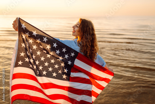 Cheerful happy woman outdoors on the beach holding USA flag having fun. USA celebrate 4th of July. Independence Day concept