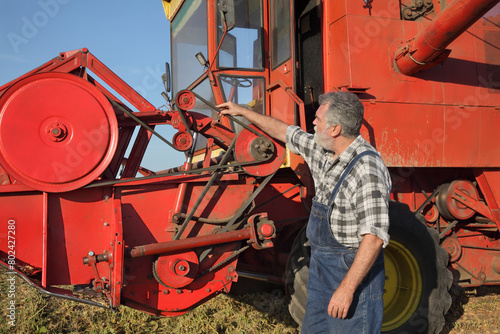 Adult farmer or mechanic touching and examining belt at combine harvester
