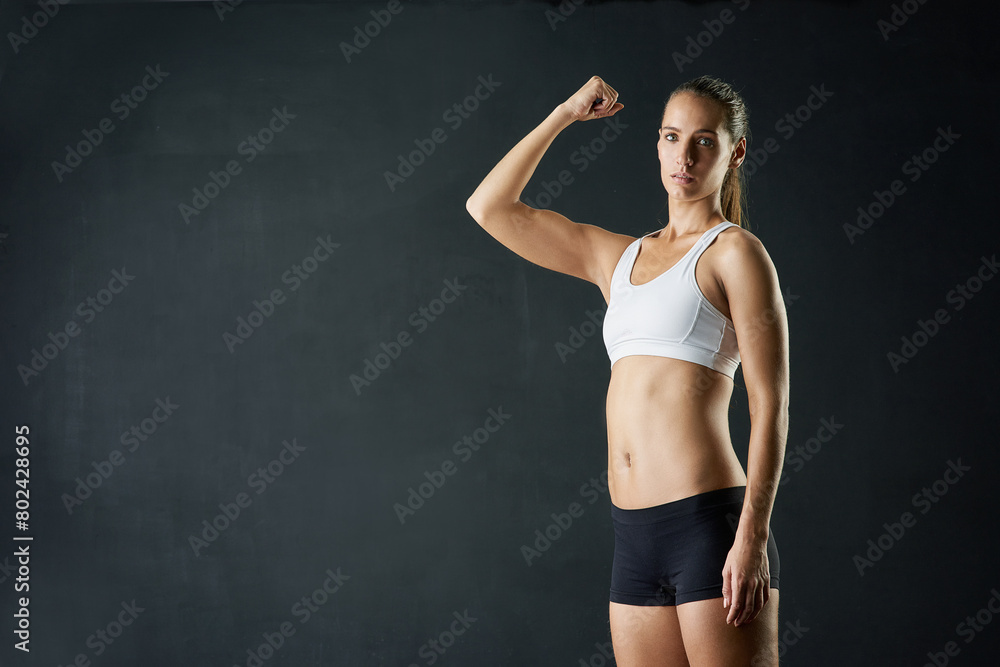 Obraz premium Fitness woman, portrait and mockup with strong arm in studio for wellness, training and muscle growth on black background. Gym, space and bodybuilder with bicep flex, challenge or body transformation