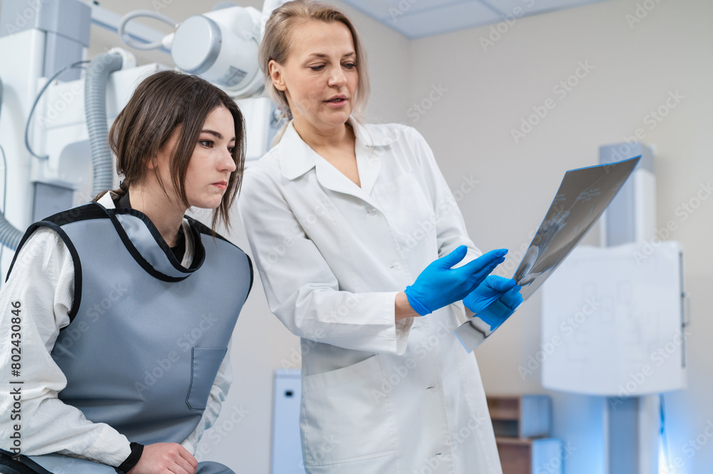 a female doctor and a young female patient look at an x-ray of hands, fingers and rejoice in the radiology room against the background of medical equipment. No bone fracture. a female doctor and a young female patient look at an x-ray of hands, fingers and rejoice in the radiology room against the background of medical equipment. No bone fracture.