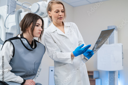 a female doctor and a young female patient look at an x-ray of hands, fingers and rejoice in the radiology room against the background of medical equipment. No bone fracture. 