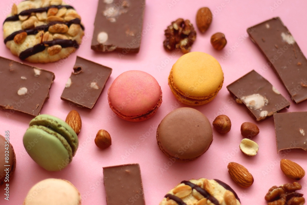 Pastel macarons, almond chocolate, peanut butter cookies and various nuts on bright pink background. Selective focus. Pastel macarons, almond chocolate, peanut butter cookies and various nuts on bright pink background. Selective focus.