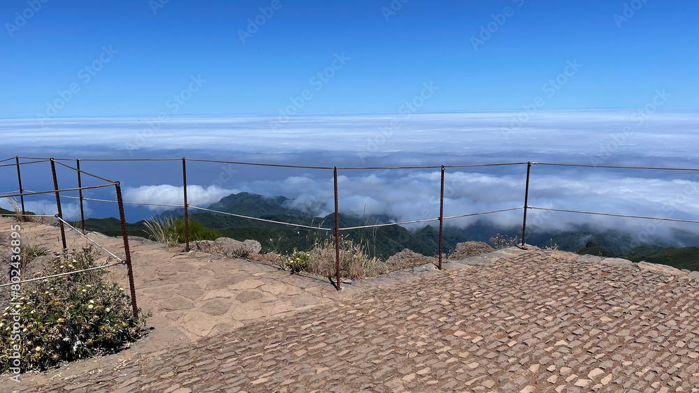 A stone-paved viewpoint on Madeira Island, offering panoramic views above the clouds with green mountains below and a bright blue sky. A stone-paved viewpoint on Madeira Island, offering panoramic views above the clouds with green mountains below and a bright blue sky.