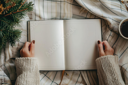 Hands holding an open blank book on a cozy blanket photo