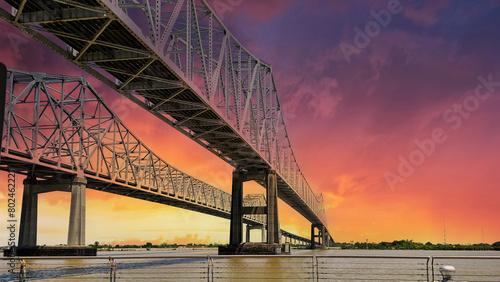 The Crescent City Connection bridge over the Mississippi River with lush green trees and plants and powerful clouds at sunset in New Orleans Louisiana USA
