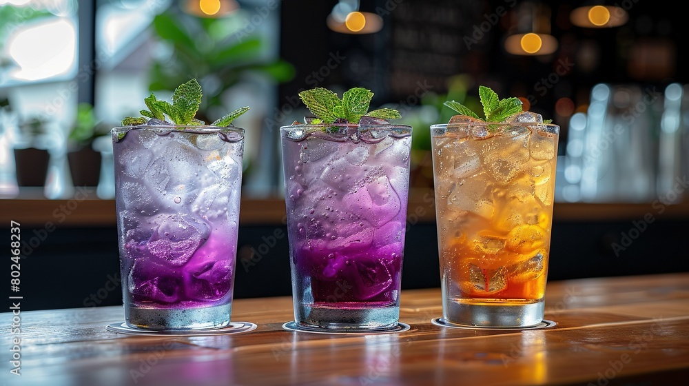 Three differently-colored drinks in glassware on wooden table beside potted plant, near window Three differently-colored drinks in glassware on wooden table beside potted plant, near window