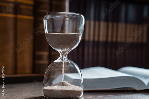 Hourglass and opened book on library table