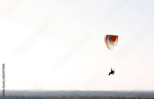 Silhouette of a man flying a motorized paraglider over a flat landscape. Extreme outdoor sports activities. Side view, negative space, copy space.