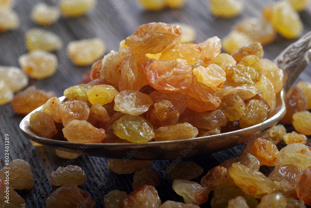 golden raisins in a spoon on a wooden table. dried grapes. close up golden raisins in a spoon on a wooden table. dried grapes. close up