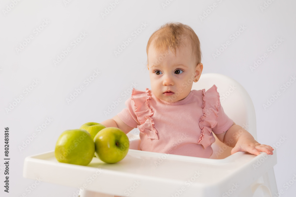 Cute baby in a baby chair nibbles apples on a white background
