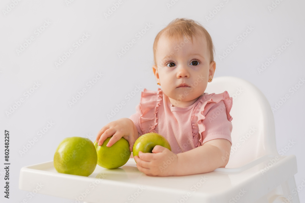 Cute baby in a baby chair nibbles apples on a white background Cute baby in a baby chair nibbles apples on a white background