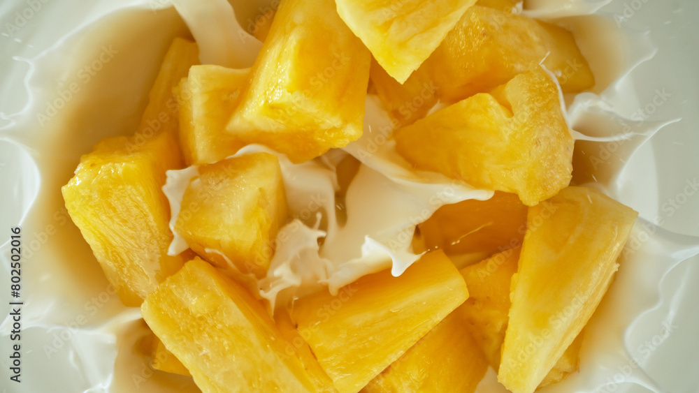 Fresh pineapple pieces falling into yoghurt cream, top down view Fresh pineapple pieces falling into yoghurt cream, top down view