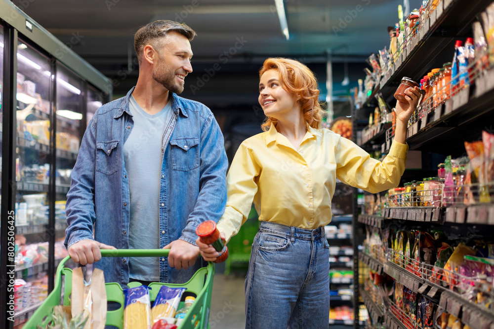 Happy European couple shopping groceries in supermarket, choosing and buying food together, standing near shelves in store aisle