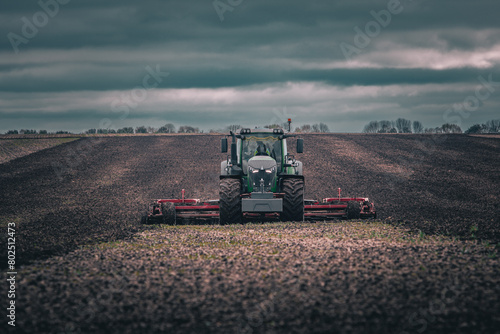 Tractor with cultivator working on a field under dark moody sky