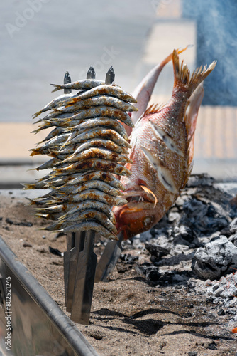 Skewers of octopus, sea bream, shrimp and sardines, grilled over a wood fire in a boat on the sand of the beach. Typical dish from Malaga, Andalusia, Spain.
