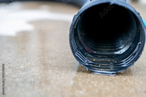 Selective focus on the front opening of a residential sump pump discharging water from the end of a flexible black hose