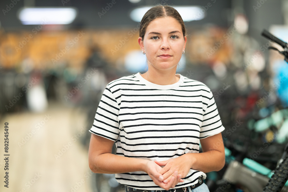 Φωτογραφία Interested young girl in casual striped t-shirt and jeans confidently walking through bicycle store, exploring variety of options and perhaps contemplating next cycling adventure
