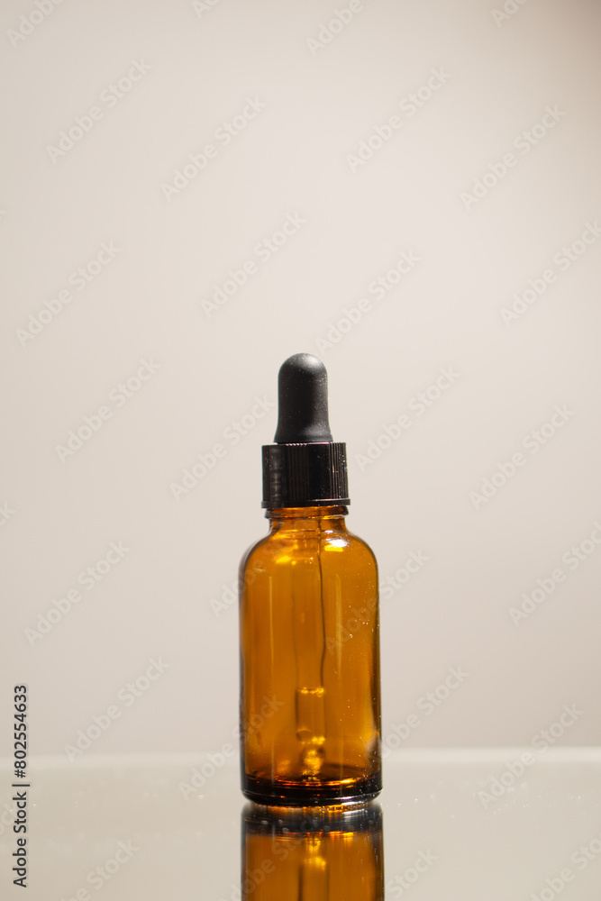 A brown bottle of an essential oil on a specular surface, with a neutral background.