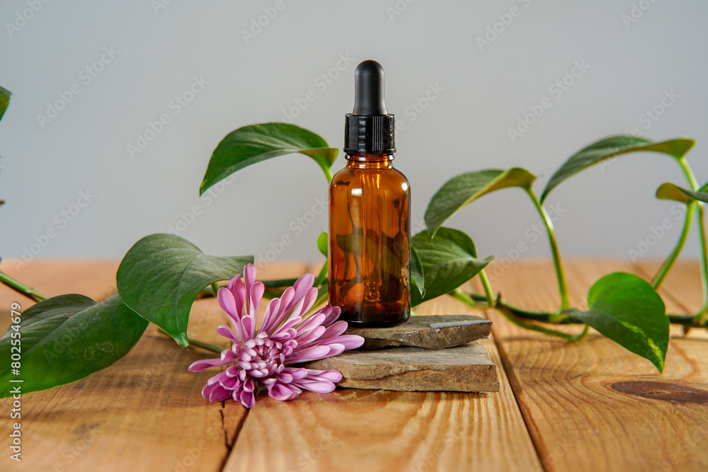 A bottle of essential oil sitting on rocks on a natural wooden table with a pink dahlia on the side. A bottle of essential oil sitting on rocks on a natural wooden table with a pink dahlia on the side.