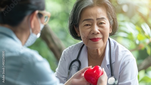 Elderly patient woman give red heart gift to Asian senior doctor in hospital. AI generated image