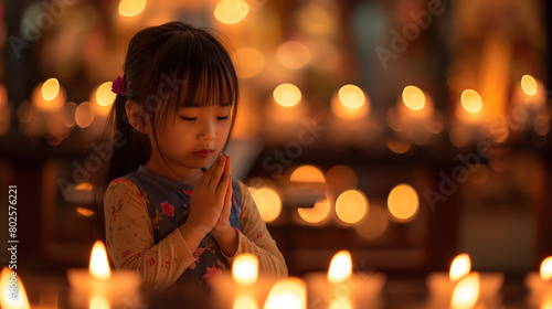 cuttle little asian girl prays in church with hands put together, candle lit background. Hope and faith concept