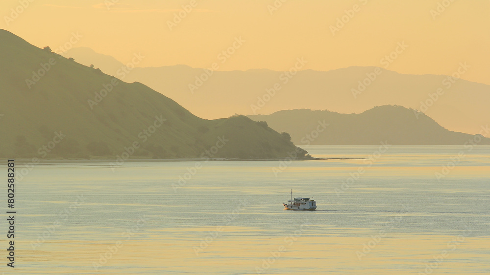 view of the sea and hills with a yellowish sky and a ship in the middle of the sea sailing on Gili Lawa land