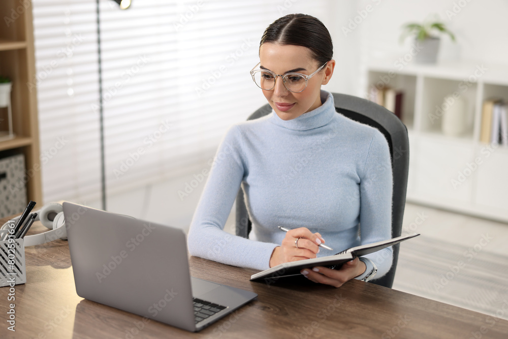 Obraz premium Young woman in glasses watching webinar at table in office
