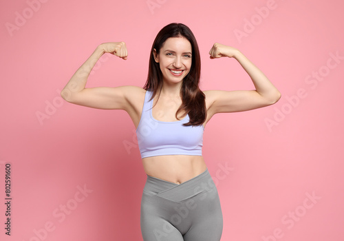 Happy young woman with slim body showing her muscles on pink background photo