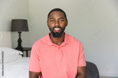 African American man wearing a pink shirt, smiling at the camera during a video call at home
