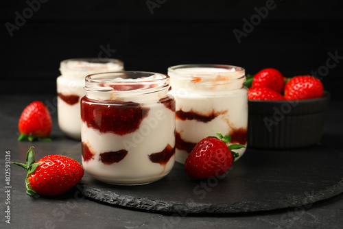 Tasty yoghurt with jam and strawberries on black table  closeup