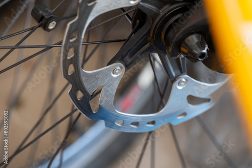 Close-up of a bicycle disc brake on a wheel with detailed view of the brake rotor and spokes, set against a blurred background