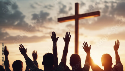 Christian worshipers raising hands up in the air in front of the cross, sunset