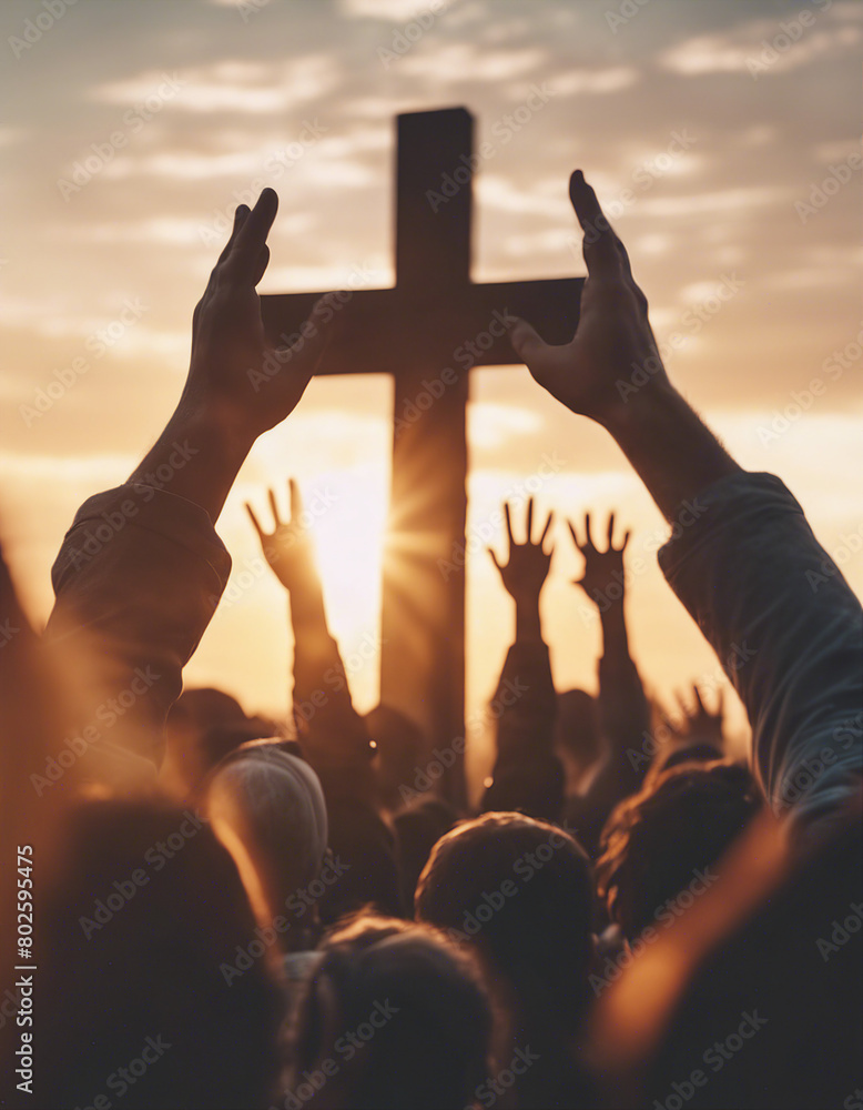 Christian worshipers raising hands up in the air in front of the cross, sunset

