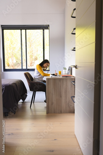 Biracial young woman wearing glasses, writing at desk at home photo