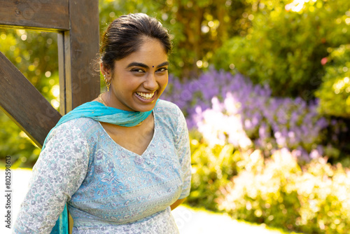 Indian young woman standing in garden, smiling brightly photo