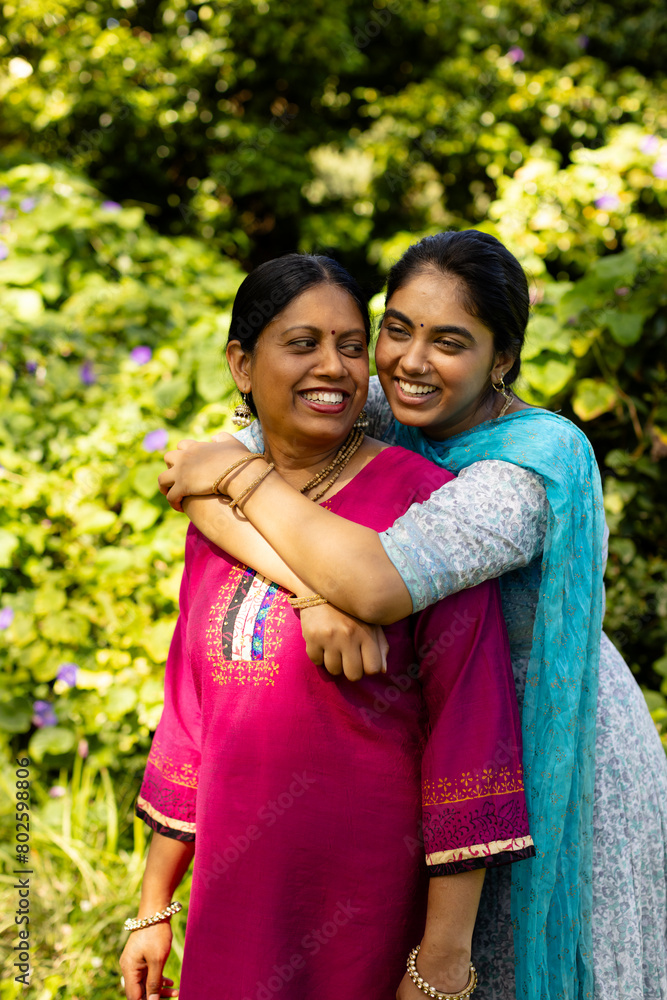 Indian mother and teenage daughter, both with dark hair, hugging outdoors Indian mother and teenage daughter, both with dark hair, hugging outdoors