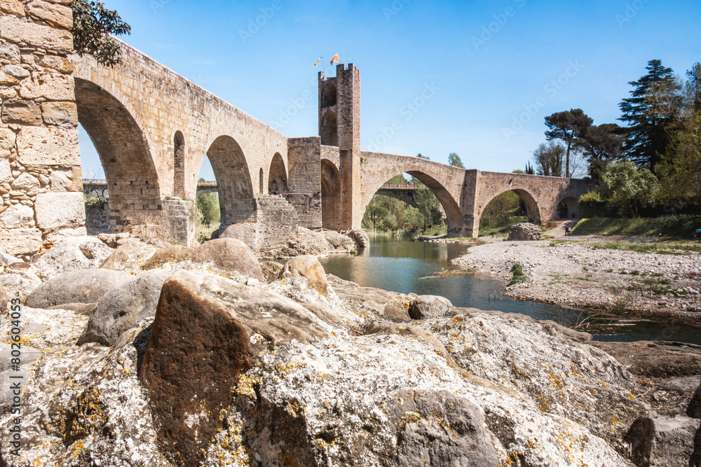 The medieval bridge of Besalú crosses the Fluvià river with a stone wall on each side.