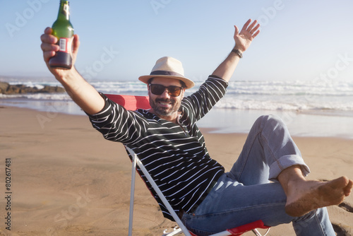 happy mature man sitting on the beach with arms up enjoying a beer and solitude in retirement  photo