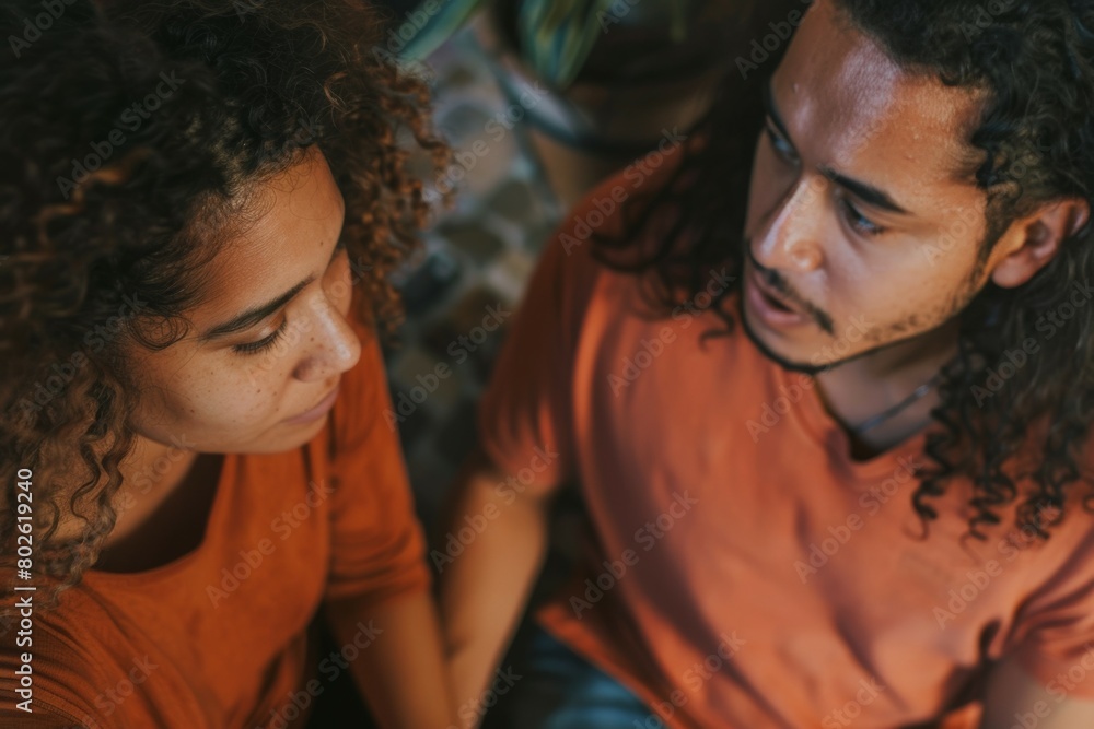 A man and woman are sitting together and the man is wearing an orange shirt A man and woman are sitting together and the man is wearing an orange shirt