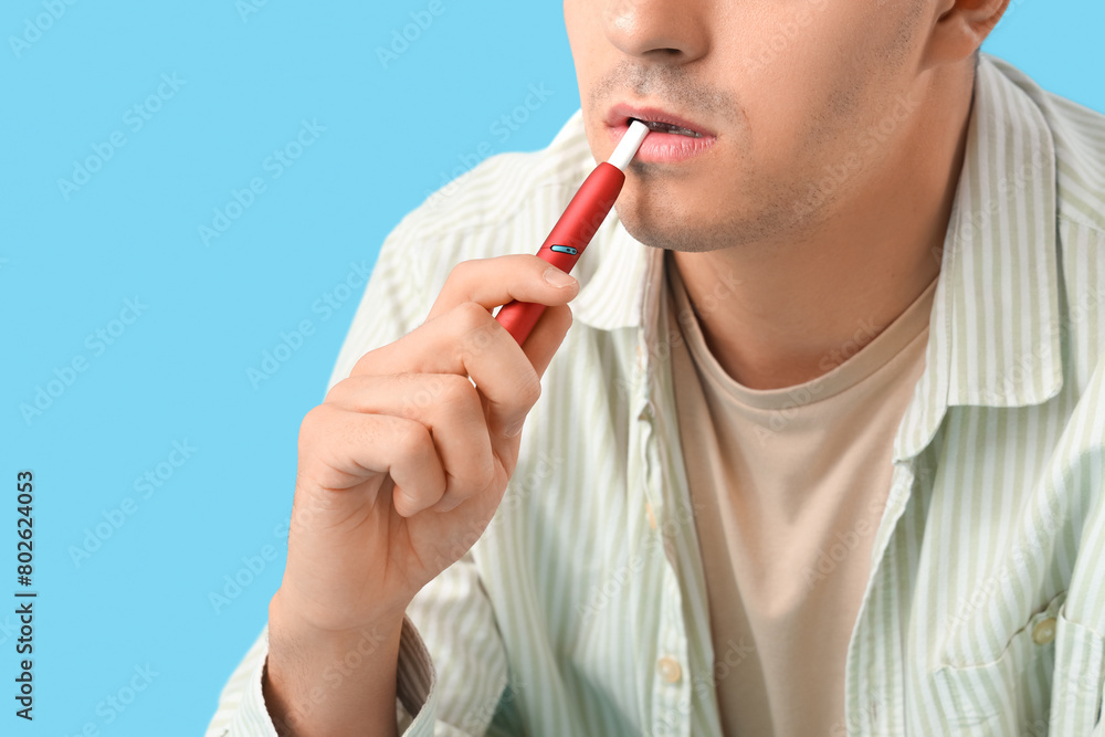 Young man smoking electronic cigarette on blue background, closeup Young man smoking electronic cigarette on blue background, closeup