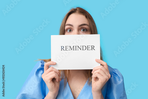 Papier peint Young woman holding paper sheet with text REMINDER on blue background