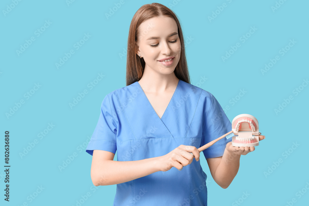 Female dentist with toothbrush and jaw model on blue background Female dentist with toothbrush and jaw model on blue background