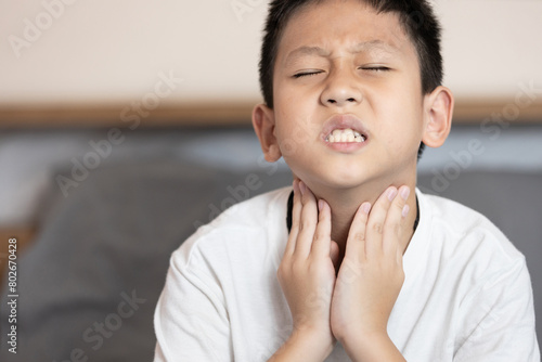 Asian child boy touching his neck,loss of the voice,hoarseness,voice is hoarse from Laryngitis or sore throat,difficulty swallowing,irritation inside throat or disease of tonsillitis,acute pharyngitis photo