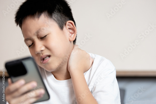 Asian boy looking at phone screen,tilting his head down for long time,Text Neck Syndrome,Smartphone or Mobile syndrome,stiff and pain in neck muscle,aching and tightness in nape of neck and shoulder photo