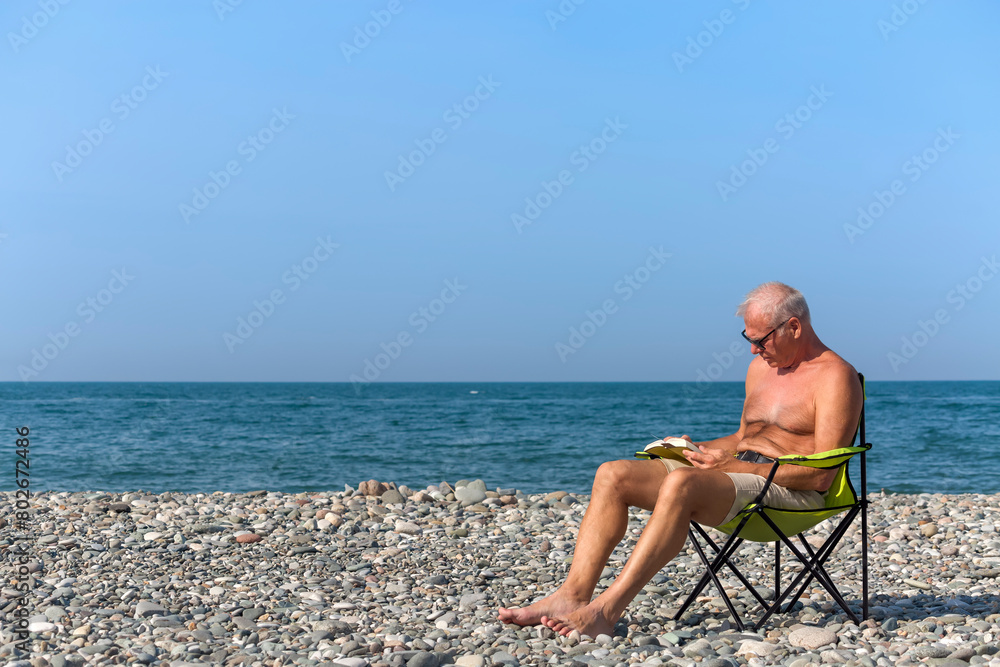 An elderly man is reading a book on the beach
