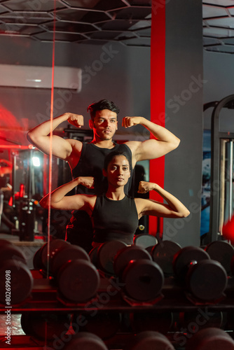 Foto Young indian couple showing muscle biceps workout at gym