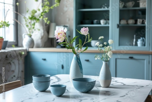 Empty and clean marble dining table in scandinavian kitchen. Modern monochrome interior with blue drawers on wooden furniture. Tablewear and vases with flowers - generative ai © Nia™