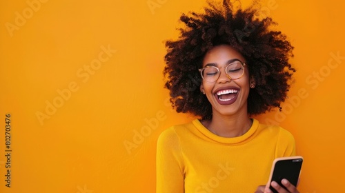 African American woman with afro hair laughing while using smartphone photo