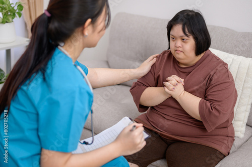 Asian female nurse or therapist Providing counseling to disabled Asian women with Down syndrome. Asian female therapist talks and encourages obese Down syndrome child with depression at home