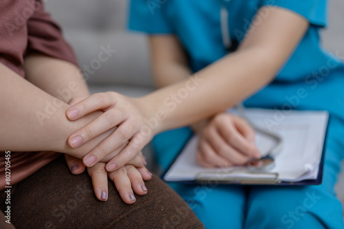 Close-up of a female nurse or therapist holding hands and giving encouragement to an obese Down syndrome child with depression at home and giving advice and talking to the sick person.